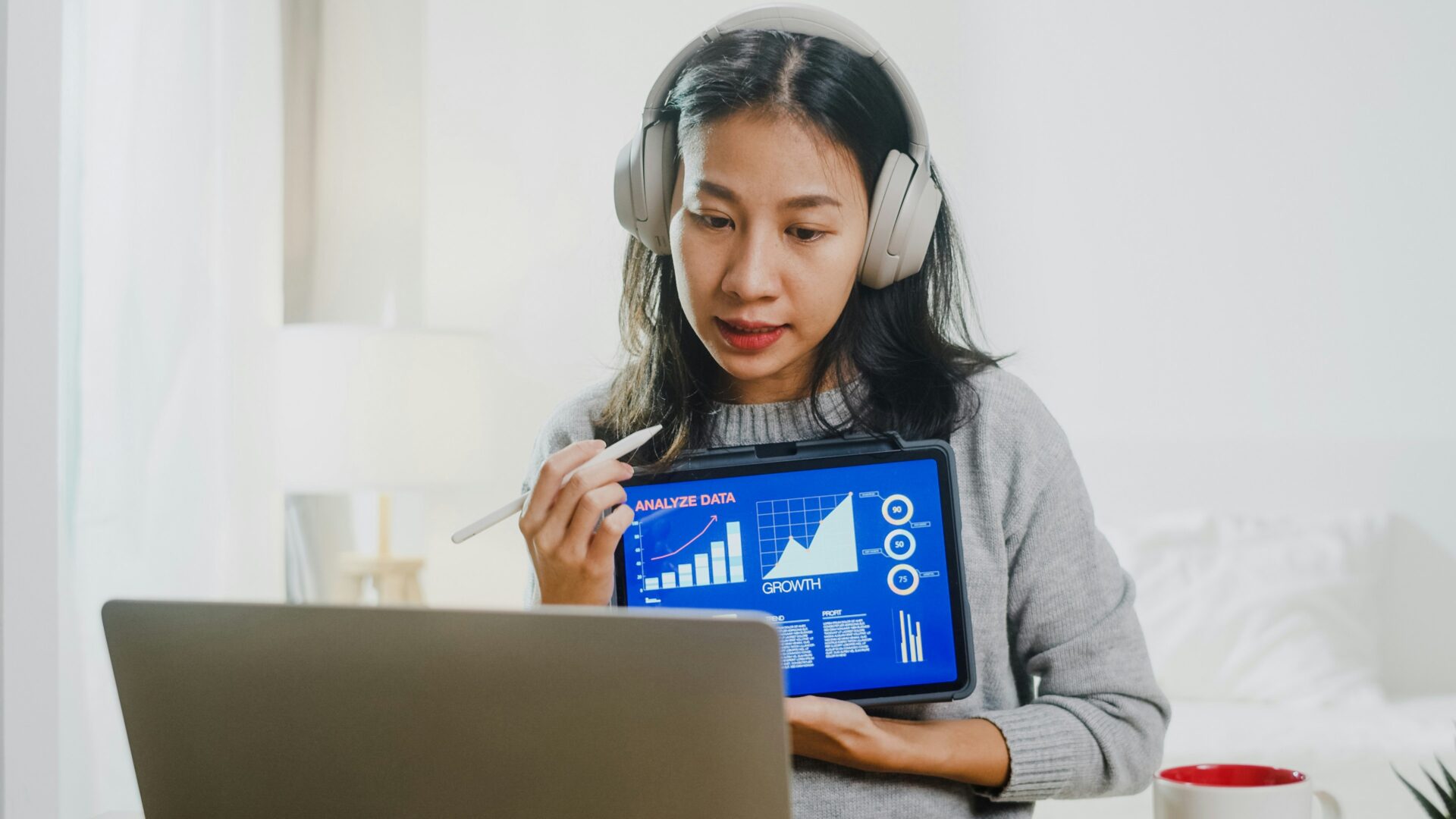 woman holding ipad with charts while on zoom call in front of laptop picture